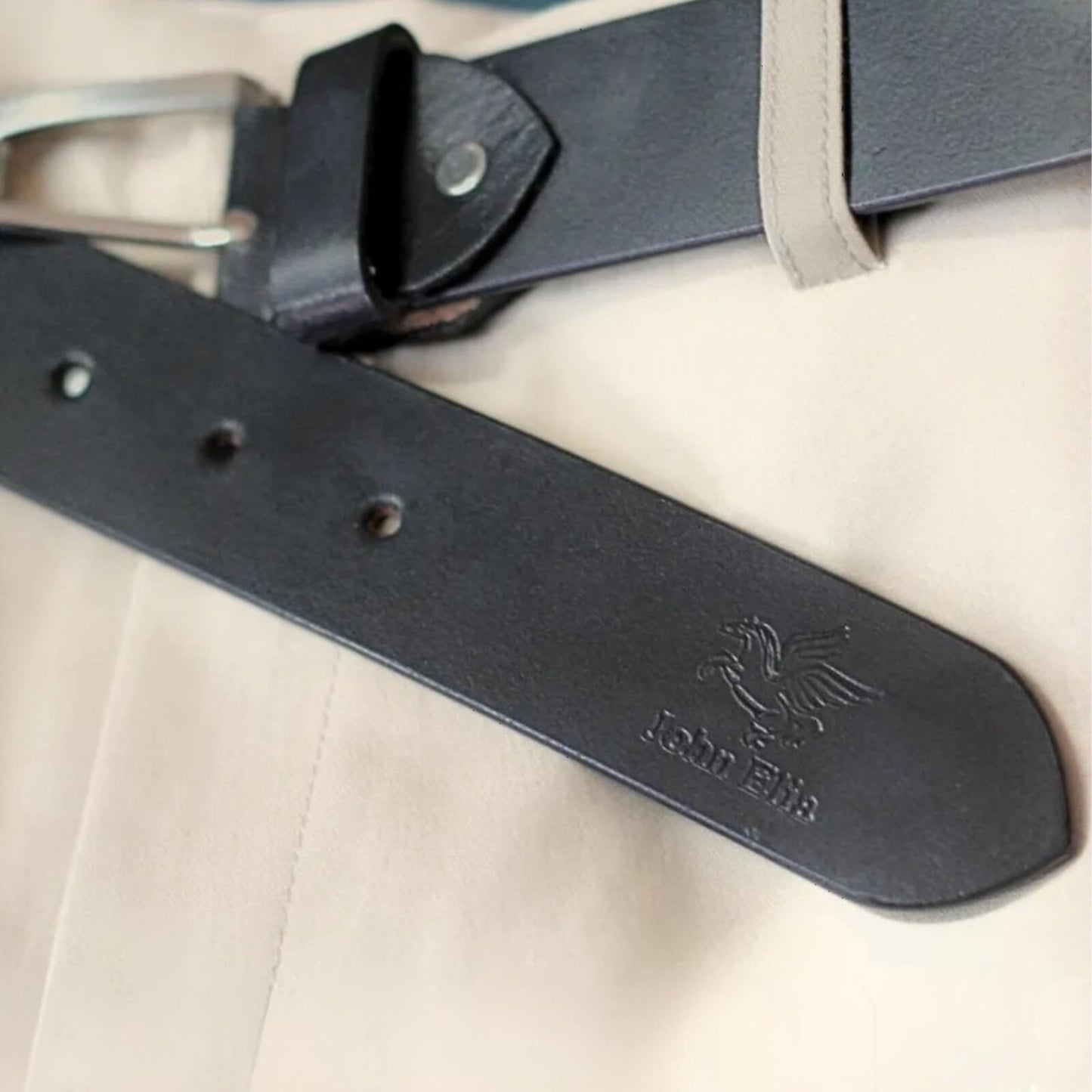 Black leather belt with a brand logo on beige fabric