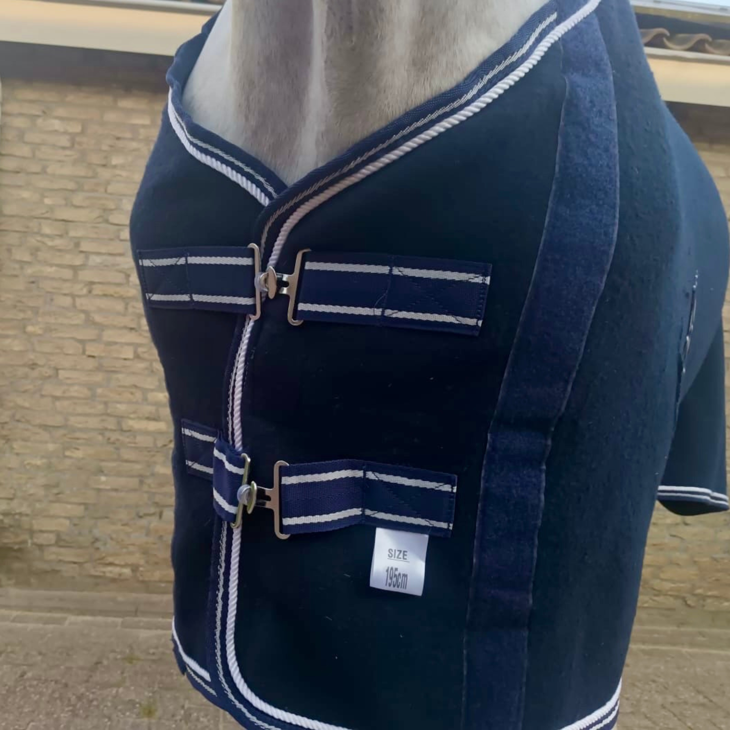 Navy blue jacket with white trim on a mannequin against a brick wall.