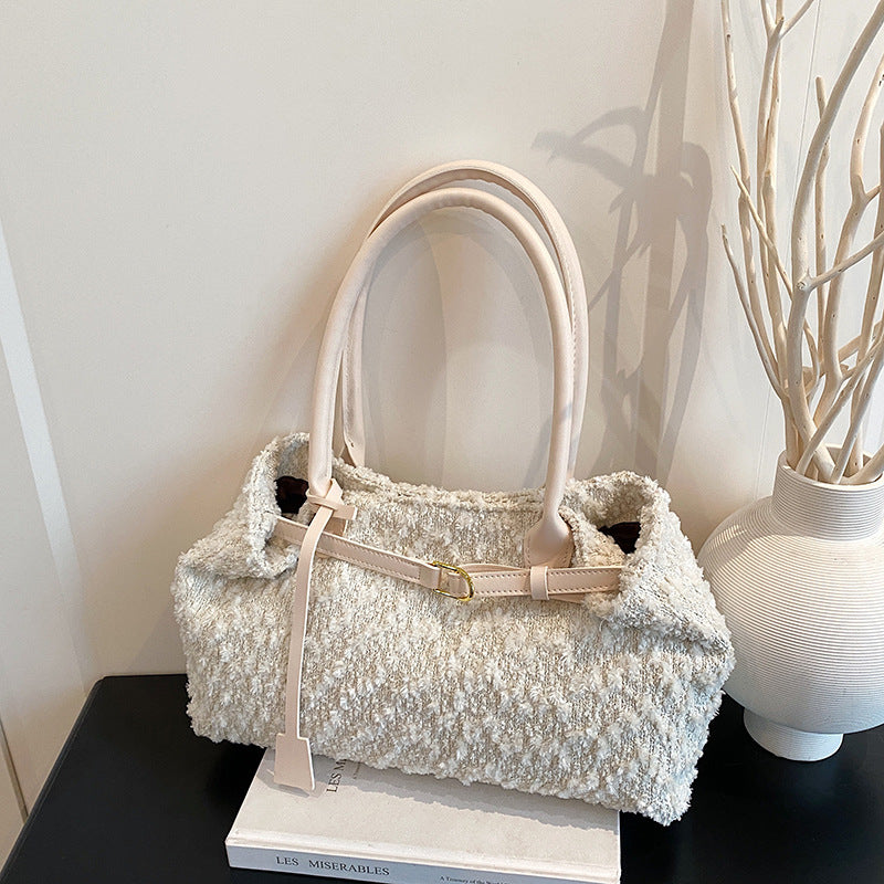 White textured handbag on a black surface with a white vase and books in the background.